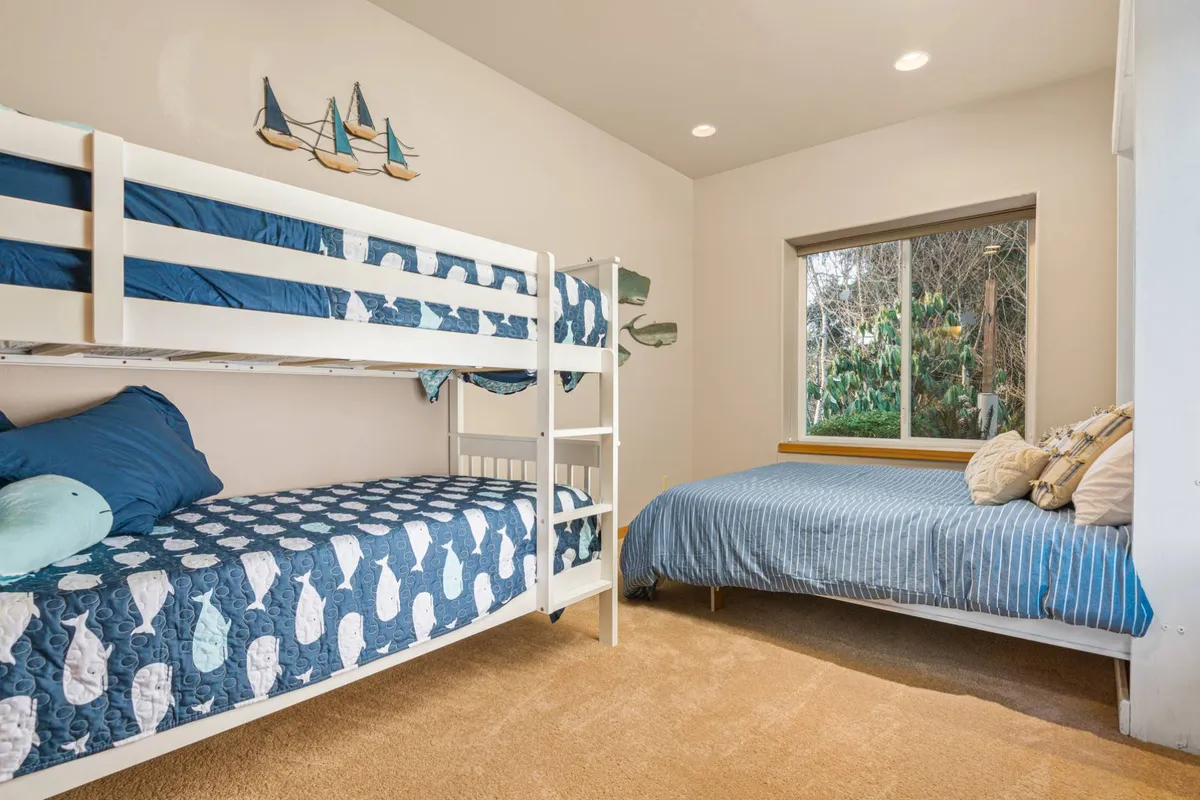 A playful and cozy bedroom with a twin bunk bed, a single bed, a window view, and decorative sailboat art. The space feels welcoming for children or friends, balancing functionality and charm.