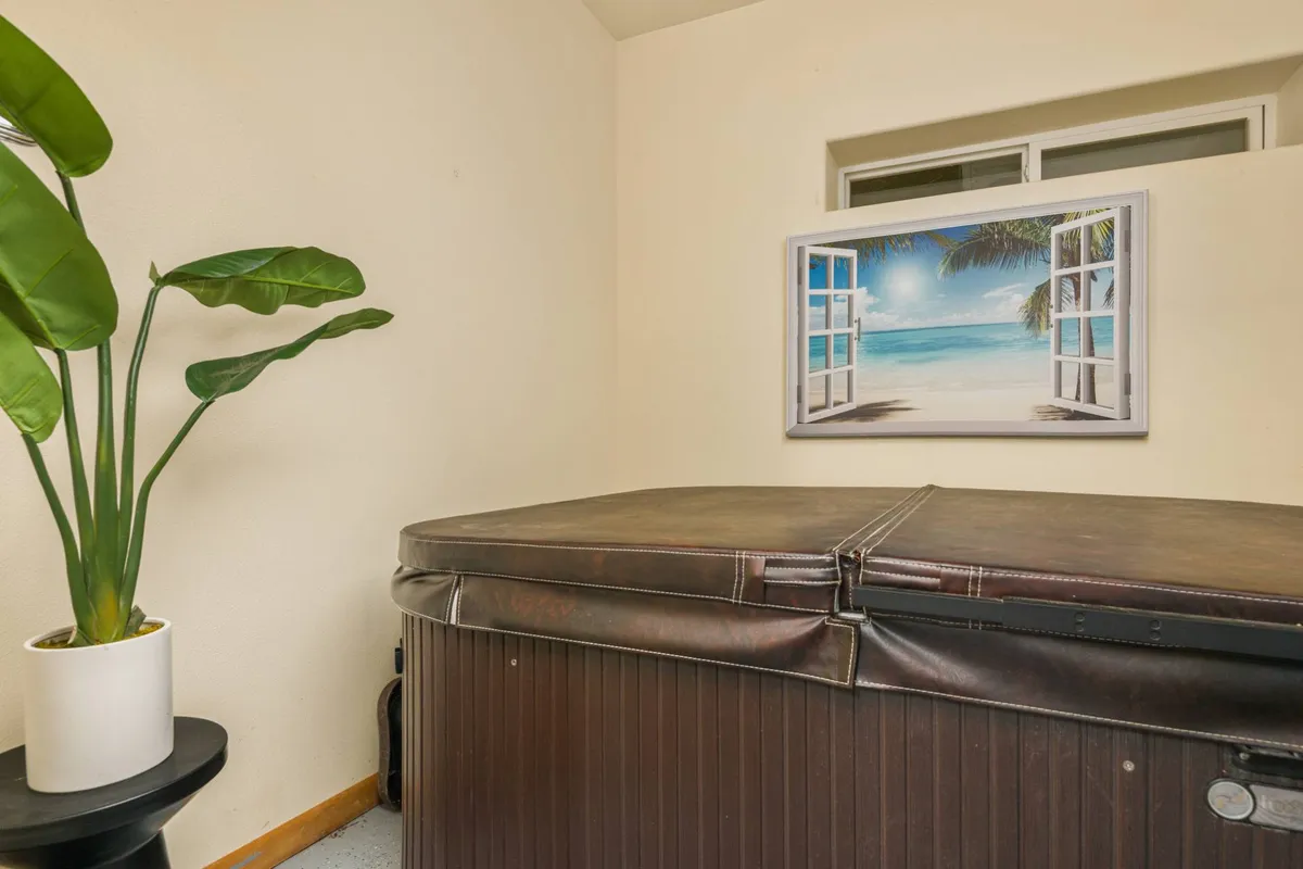 This image shows a tranquil indoor hot tub area with a potted plant and beach landscape artwork on the wall. The tub is surrounded by clean tiles and cozy accents, providing a relaxing and welcoming atmosphere ideal for unwinding alone or with company.