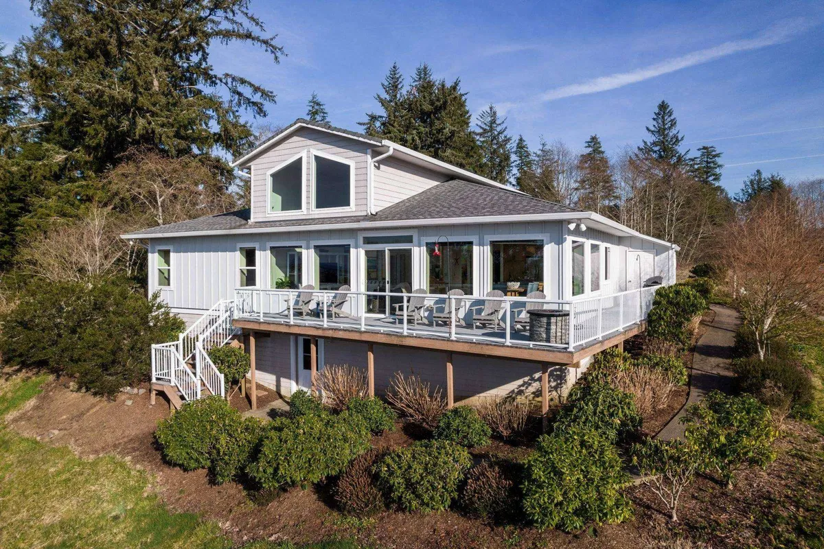 A view of the spacious deck, framed by large windows and lush greenery. The deck is set up for outdoor relaxation or socializing and highlights seamless indoor-outdoor living. The overall mood is welcoming and serene, with clear cues that the deck is an extension of the main living space.