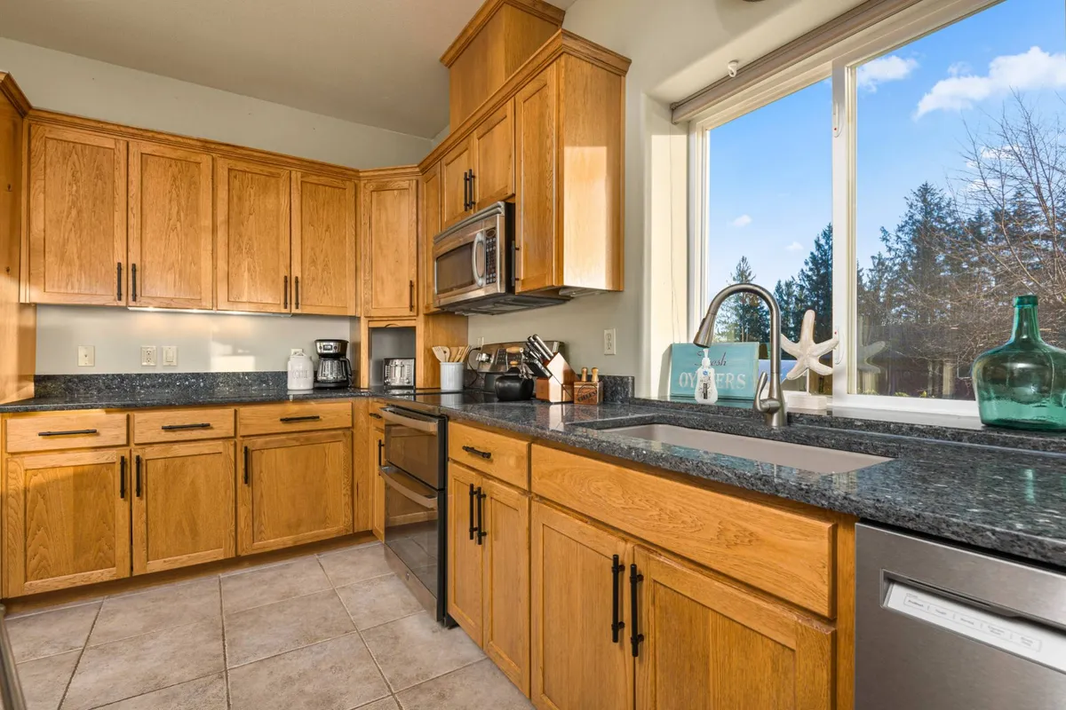 A modern, inviting kitchen with wooden cabinets, granite countertops, stainless steel appliances, and a large window—ideal for meal preparation and group dining experiences.