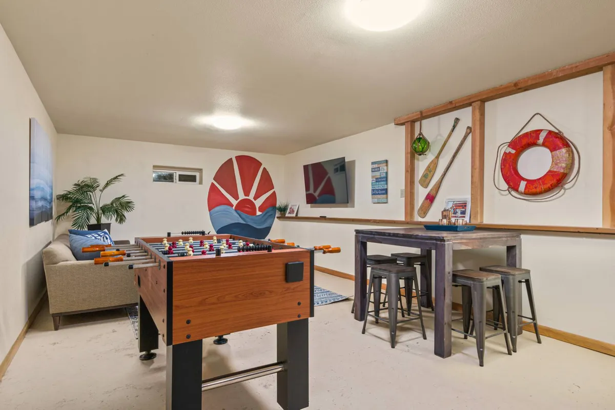 A foosball table takes center stage in a cheerful, colorful corner with wall art and a bar-style table with stools in the background, inviting both play and conversation. The mood is lighthearted and sociable.