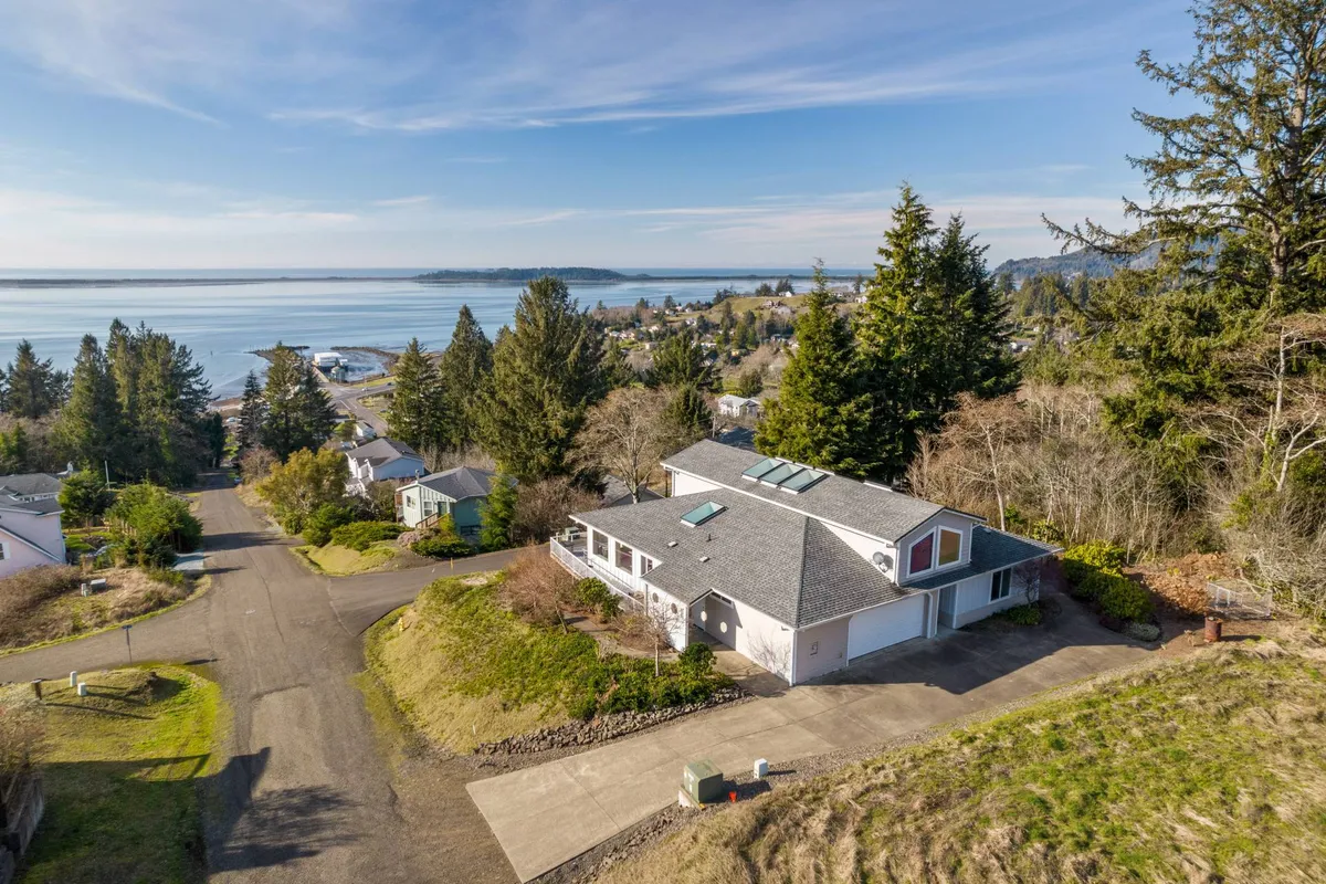An exterior view of the house nestled by the waterfront, framed by trees and a quiet road. The spacious yard invites family gatherings, while the tranquil water hints at both relaxation and outdoor fun.