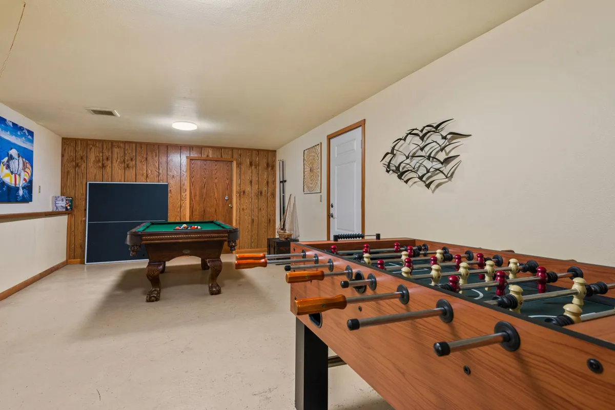 A wood-paneled game room featuring a pool table, a foosball table, and playful decorative elements like a fish sculpture. The scene suggests a relaxed, welcoming space for gatherings and spontaneous game nights.